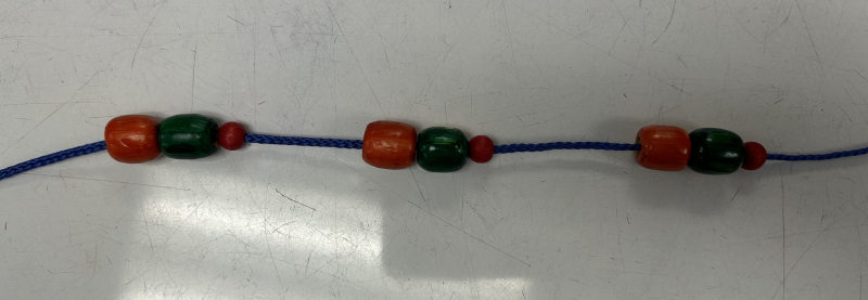 Examples of students making their own necklace with beads to create a repetitive sequence. Example is orange bead, green bead, orange bead, space, orange bead, green bead, orange bead, space, orange bead, green bead, orange bead.