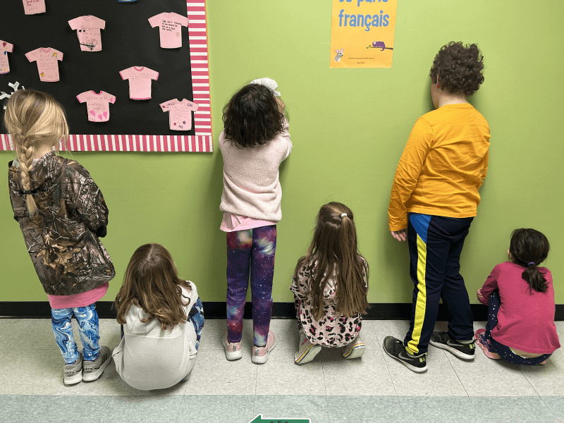 Children in a classroom. Their body form a sequence, from right to left: kid one is kneeling, kid 2 is standing, kid 3 is kneeling, kid 4 is standing, kid 5 is kneeling, and kid 6 is standing. 