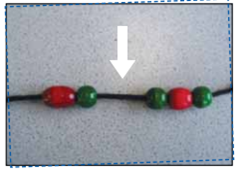A sequence of repetitive patterns repeated 3 times, beads forming a necklace. The pattern is red oval bead, a green sphere bead. A space is left to show where the missing bead should go. A white arrow is used to show the space.