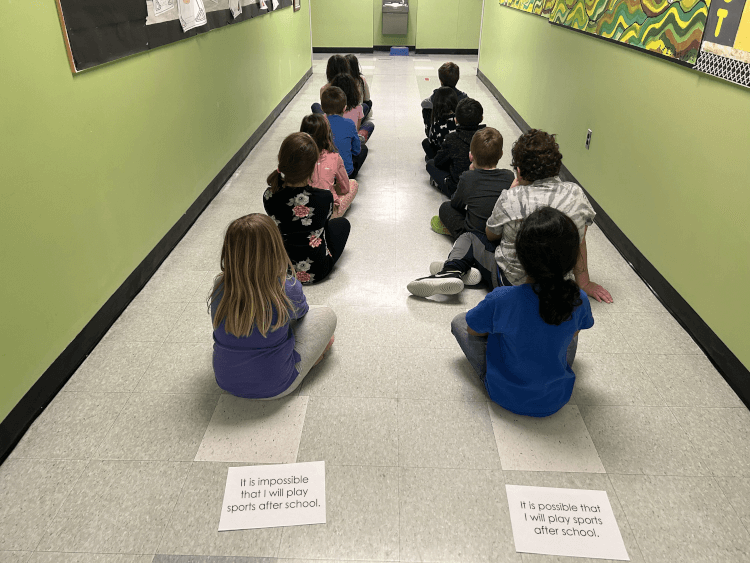 Photo of students sitting on the floor, one behind the other, forming two lines, each represented by a statement. 
