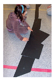 Une élève est assise par terre, elle manipule des figures en cartons de grandes tailles.