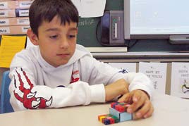 Un élève travaille avec des prismes en papiers et des prismes en cubes emboitables.