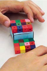 Un élève travaille avec des prismes en papiers et des prismes en cubes emboitables.