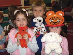 Three children, including a girl wearing an animal mask, are holding a stuffed animal.