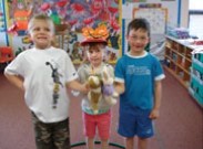 In a classroom situation. There are three children are side by side, they compare the length of their stuffed animals.