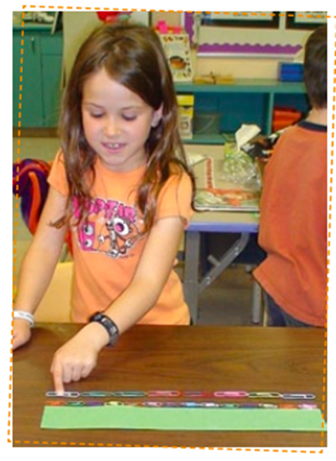 A student measures the length of a box using paper clips. The first line is made up of 14 small paper clips. The second line is made up of 8 large paper clips