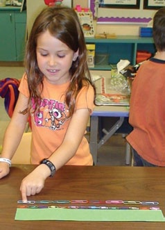 A student uses small and large paperclips to measure a carboard.